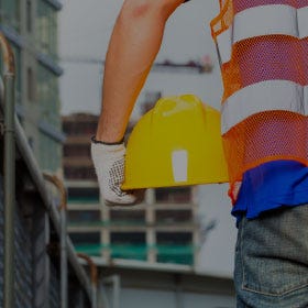 Person on Jobsite Wearing Safety Vest and Holding Yellow Helmet person on jobsite wearing safety vest and holding yellow helmet